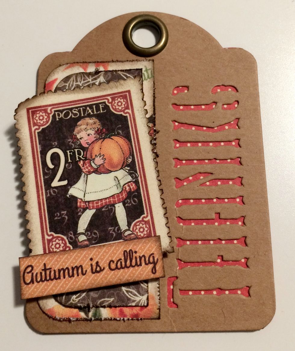 With a second red dot thanks tag, foam square a stamp on an angle overtop of brown floral piece. Roll the top left corner down. To finish, adhere "Autumn is" to the bottom left of the stamp.