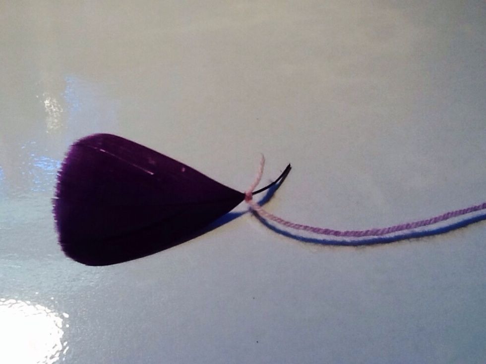 With a separate piece of yarn (15-25cm) tie the bottom to the base of your feather. Make sure to thread the end of your yarn through a needle, as you will be stringing in beads.