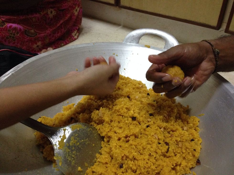 With help of both hands press the mixture making round ladoos (must do it fast before the mixture cools down).
