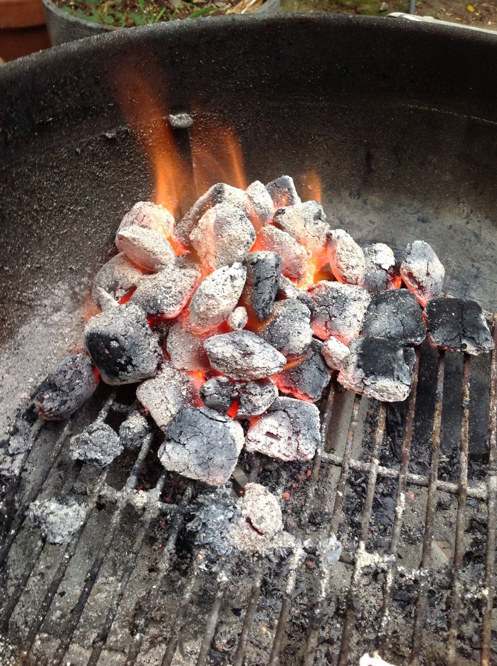 With long tongs arrange charcoal into a pile.