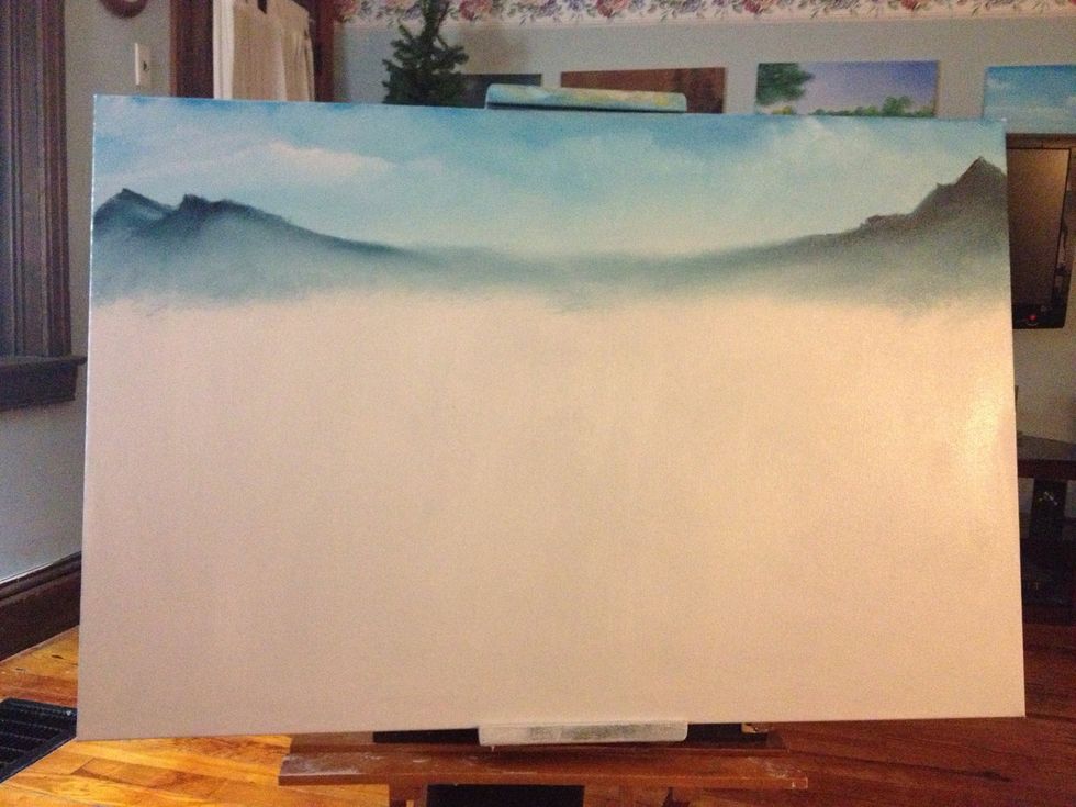 With some white and a tiny amount of red, make some clouds in your sky. Use a clean dry chip brush to blend into the sky. Then take a knife and add dark green and blue to knife in your mountain.