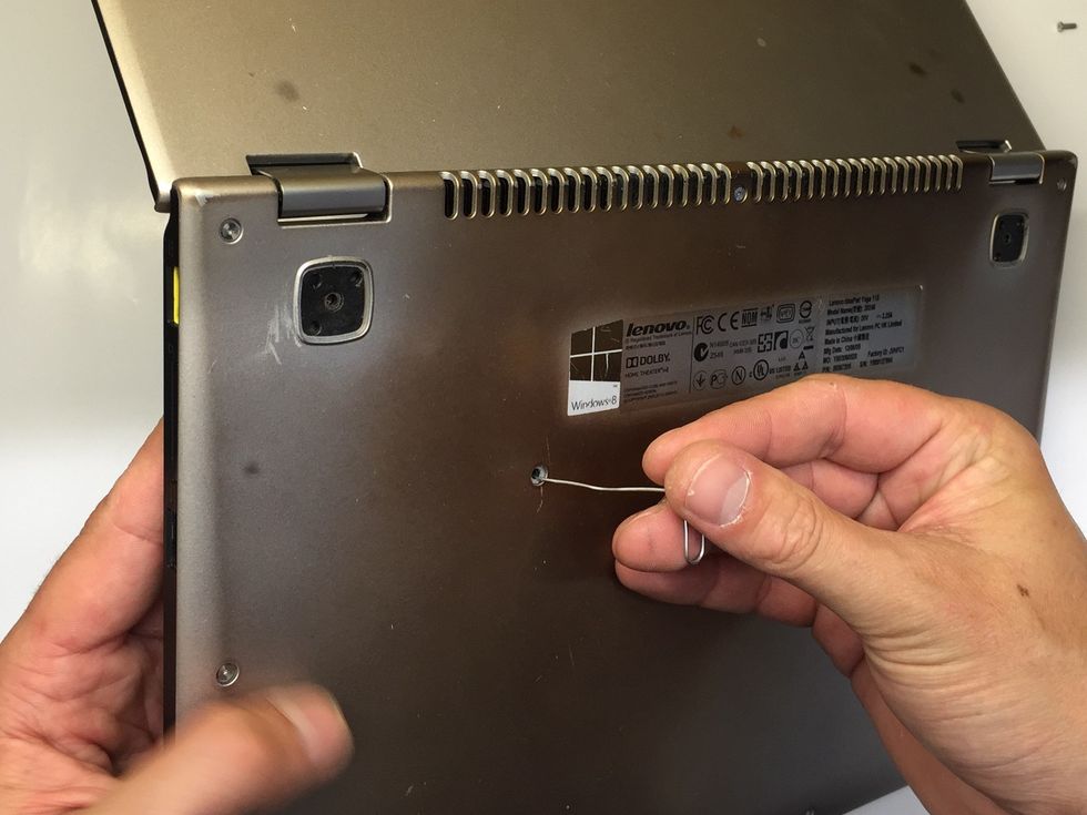 With the lid open & the laptop raised of the surface carefully push the paperclip through on of the two middle holes, this will push the keyboard out from the other side