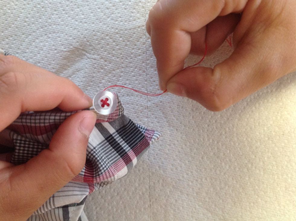 With the needle and thread in between the material and button, tightly wrap the thread around the stitching under the button three times.