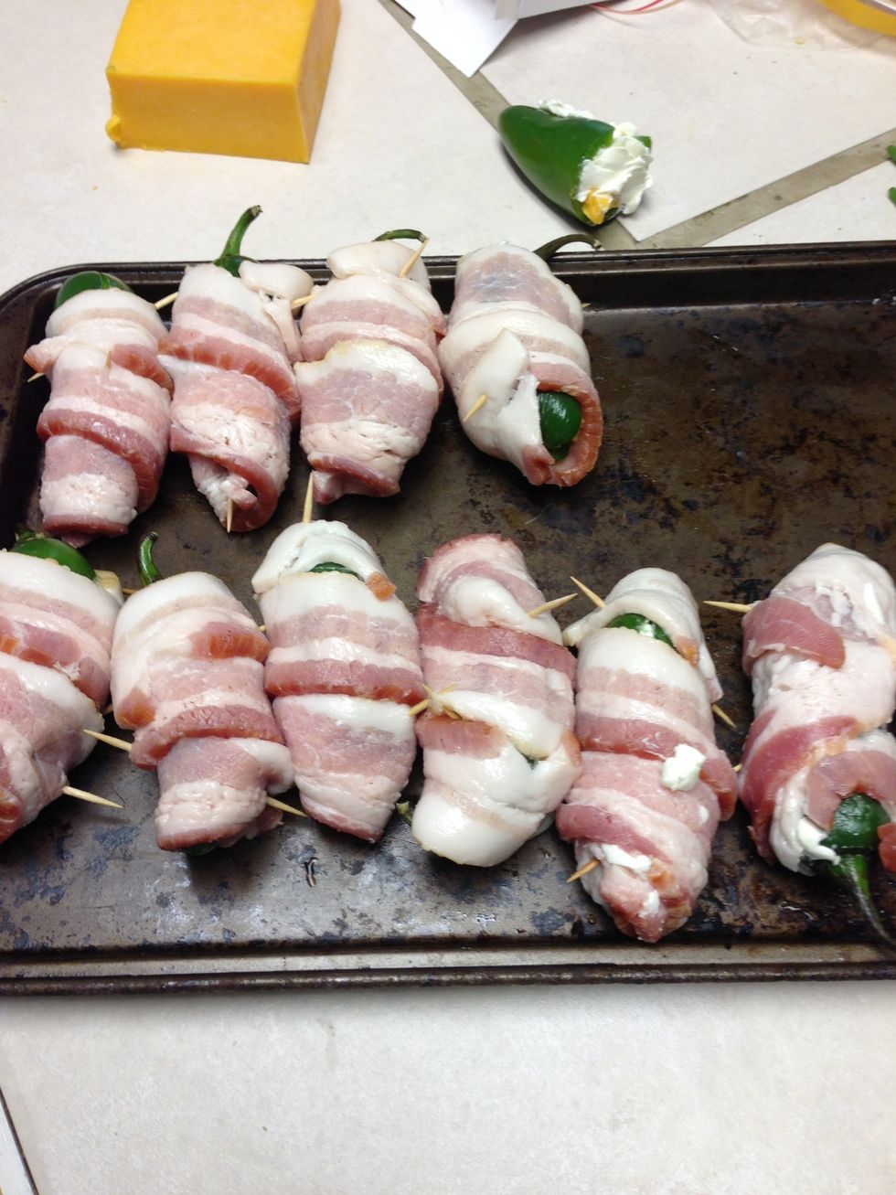 Wrap bacon around jalape\u00f1os. Use toothpicks to hold edges of bacon to the jalape\u00f1o. Try to cover as much of the cheese as possible.