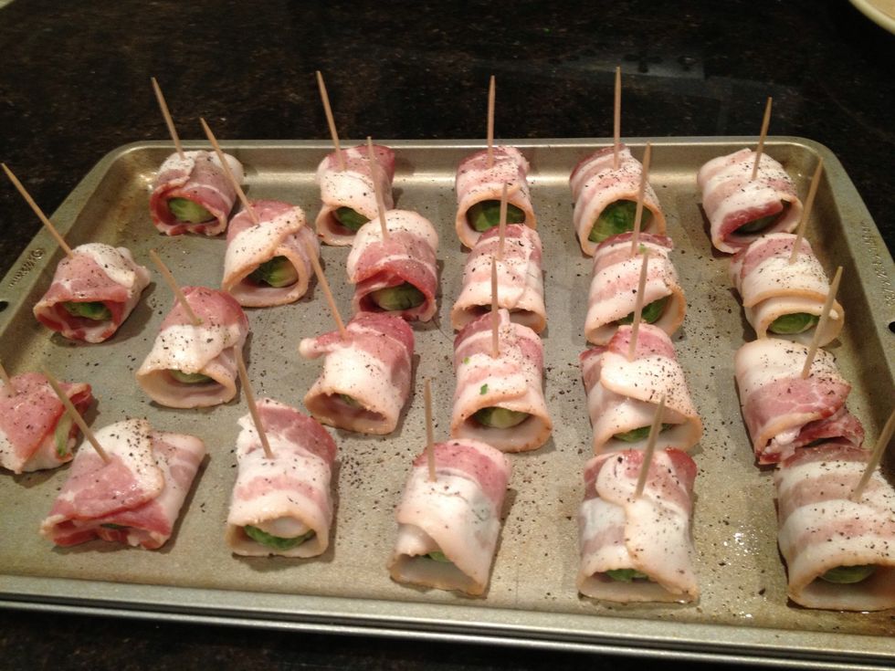 Wrap one sprout in bacon and hold together with toothpicks. The toothpicks are soaked in water to prevent them from burning in the oven. Place on greased baking sheet and sprinkle with pepper.