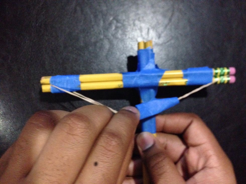 Wrap tape around the rubber band in the center to form a sling or a pouch for the projectile. Don't tape the rubber band to the body of the crossbow or you don't be able to draw it back