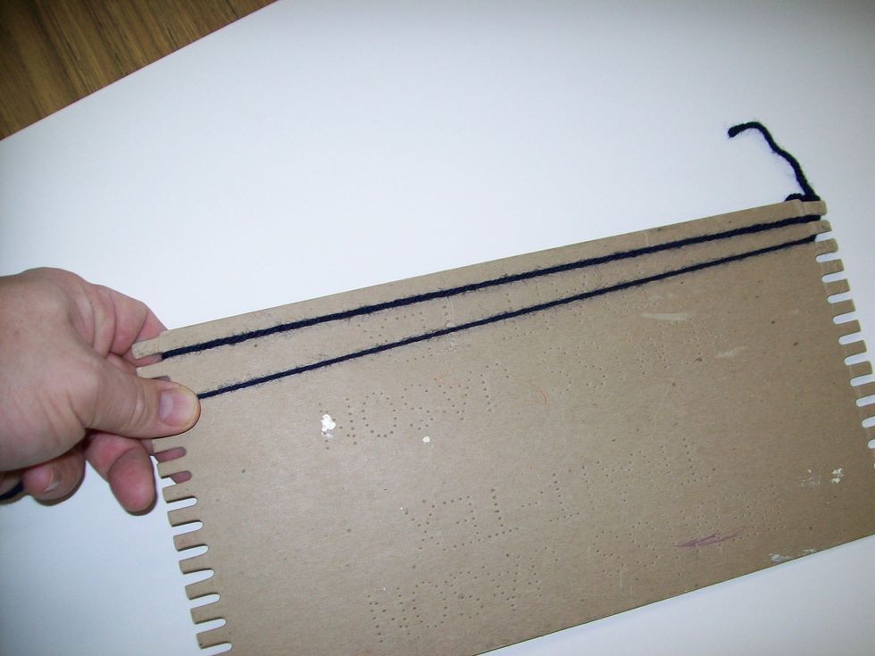 Wrap the other end of the yarn down between the 1st and 2nd tooth of the loom at the bottom. Wrap it around the back and around the top between the 2nd and 3rd tooth.