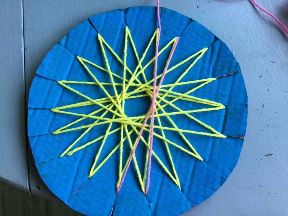 Wrap the yarn around the back of the cardboard and pull it through the slit to the left of the first slit. Pull the yarn across the front of the cardboard and pull it through the next slit