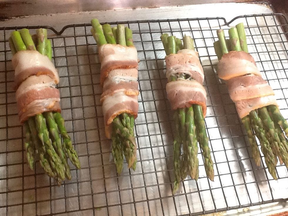 Wrap with the bacon and place the bundles on to a wire wrack with a pans under it. Place in a preheated 400 degree F. oven. Bake until the bacon is brown.