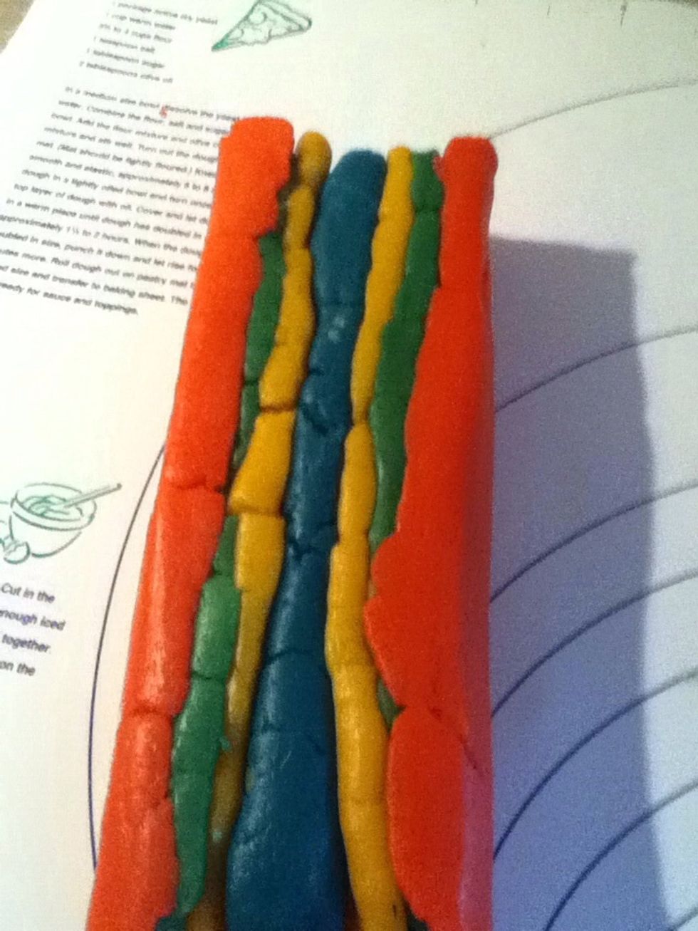 Wrap yellow dough around blue dough, wrap green dough around yellow dough and red dough around green dough. When your done wrapping the doughs it should look like a thick hot dog.