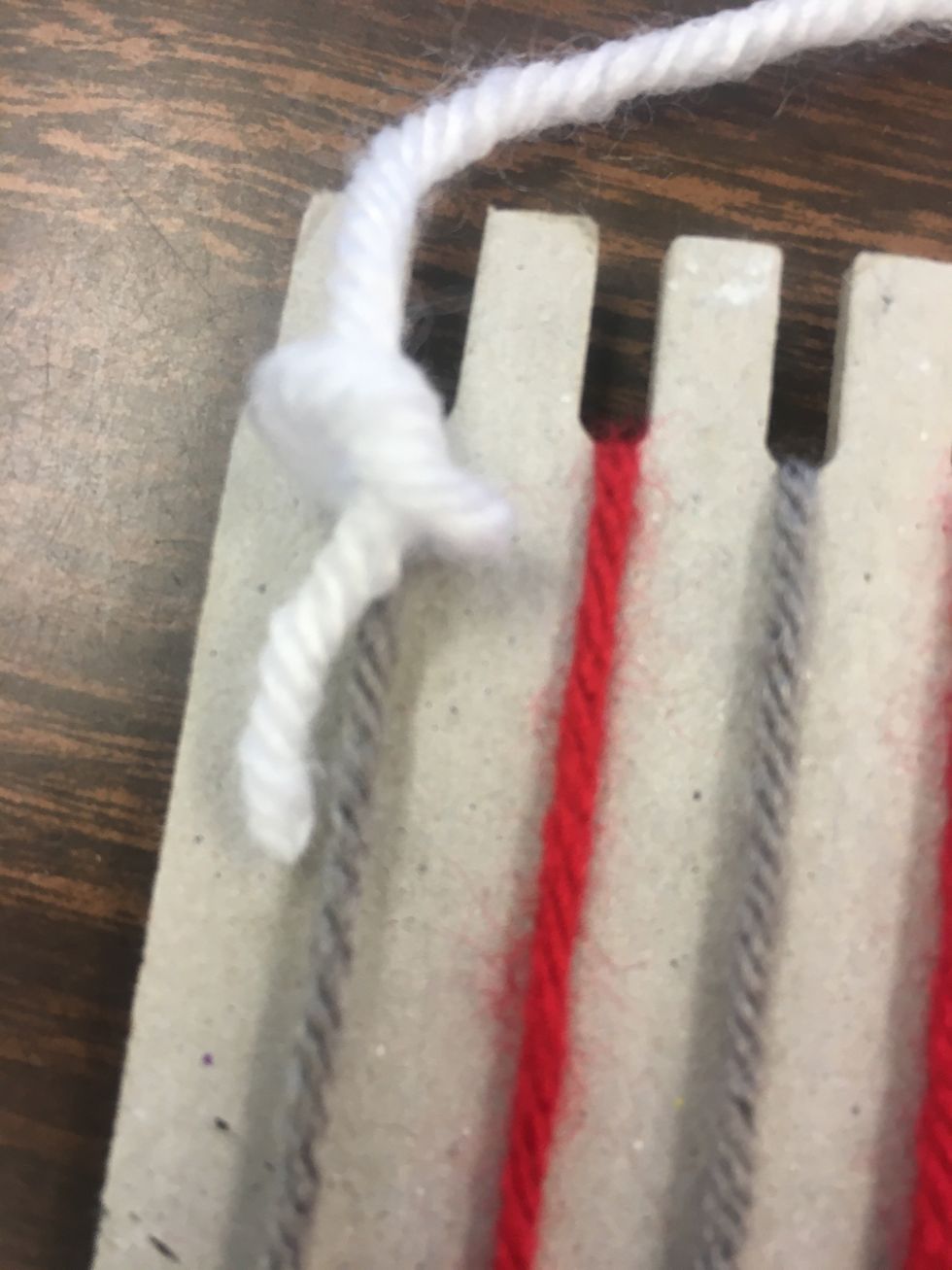 You are ready to begin weaving. Choose the first color that you would like to start with. Cut an arms length piece of yarn. In the top right corner of your loom, secure this yarn with a small knot.