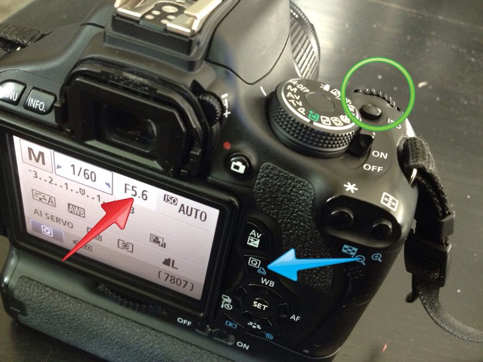 You can change the aperture (red arrow) by holding down the Q button (blue arrow) and adjusting the dial by the shutter button (green circle)