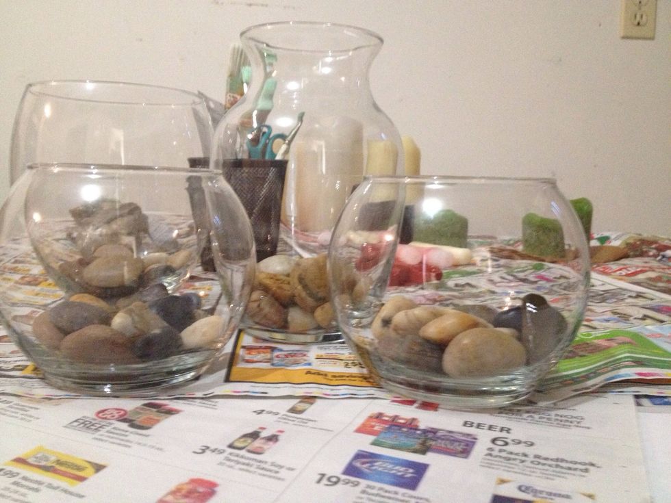 You can get all sorts of clear glass vases and glasses and bowls from dollar stores. Fill the bottom with sand, pebbles, and stones. This is your base. You can buy or gather your own.