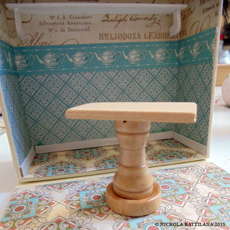 You can make tiny additions for your tea house. This shelf is a tongue depressor cut to size. The table is a checker, chess rook and domino stacked and glued together.