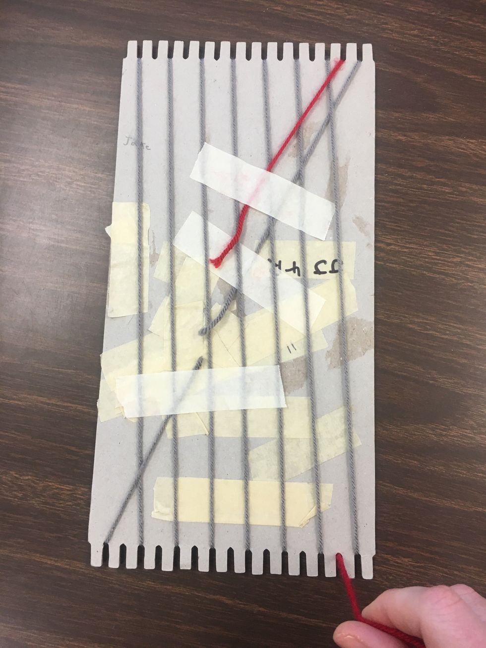 You can now use your other color yarn and repeat exactly what you did with the first yarn, but hitting the opposite notches. Secure your yarn on the back with masking tape and begin wrapping.