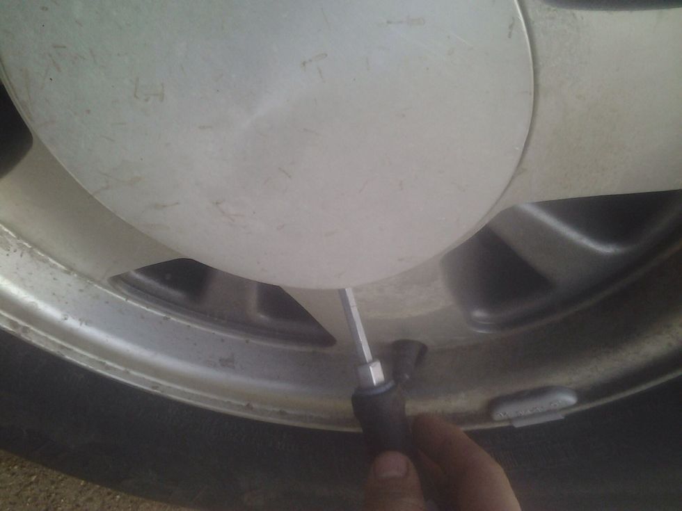 You can use a screw driver to pop the center cap off the wheel.