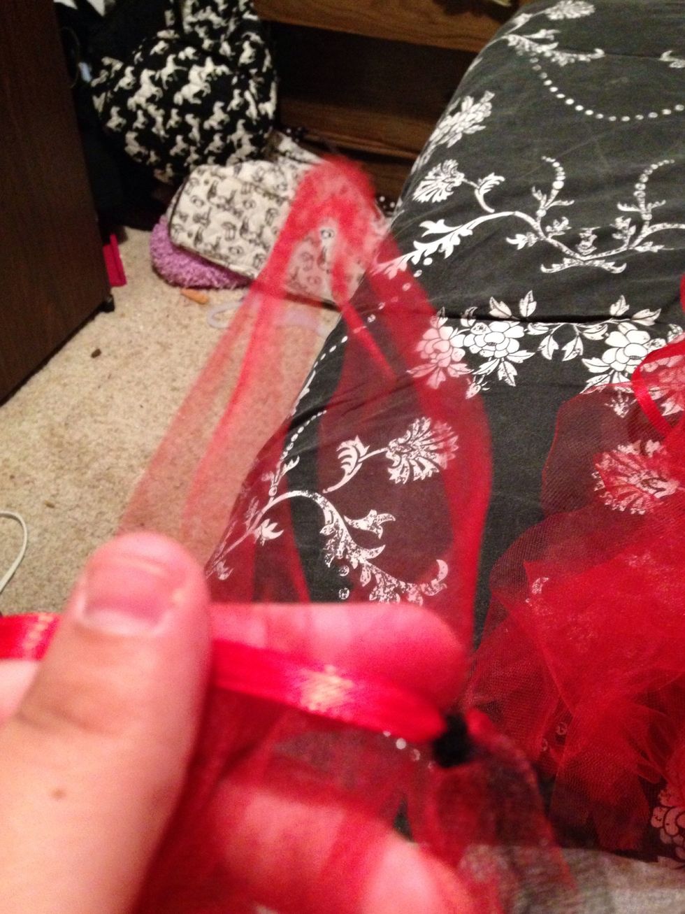 You take and hold the tulle in one hand with the looped side up.. Lay the ribbon over the top and pull the bottom through