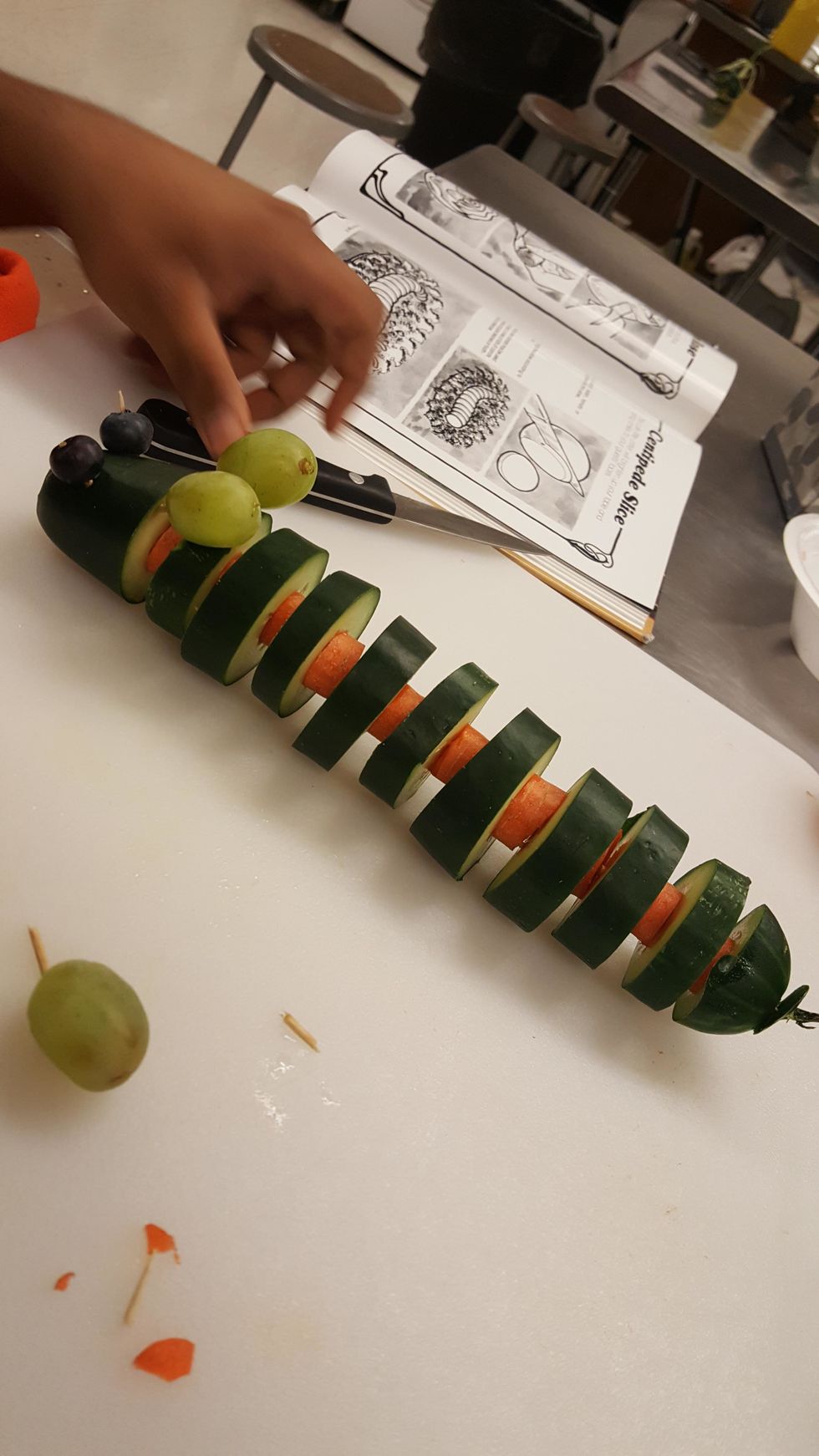 You will then take two grapes and two toothpicks and apply them at the second to last slice of cucumber and apply them for ears. And then will apply two blueberries for eyes at the end with toothpicks