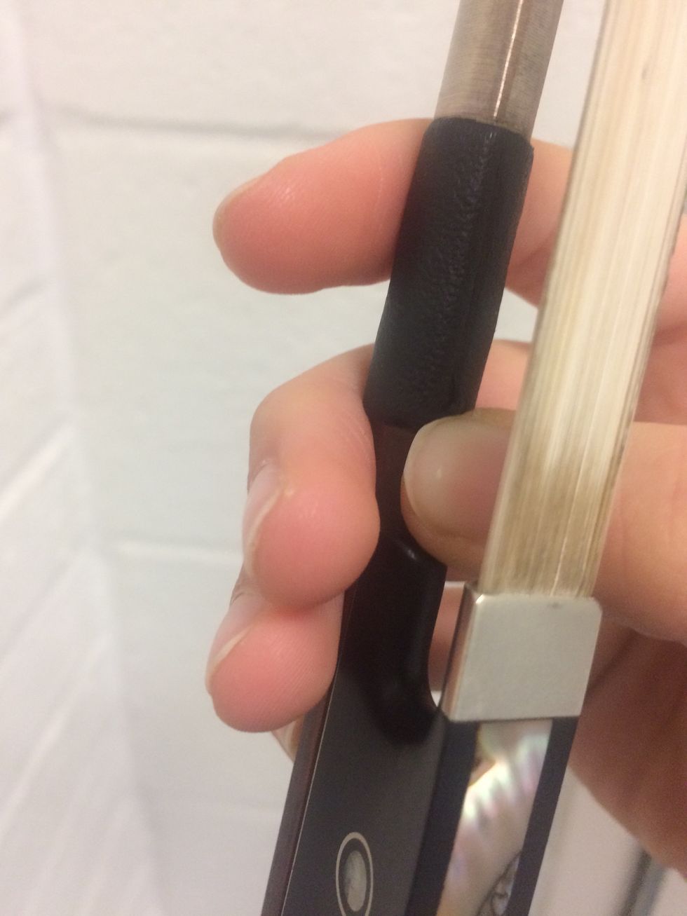 Your thumb goes under the bow between the bow hair and the stick. It should be between the leather casing on the bow and the frog(the very bottom of the bow).